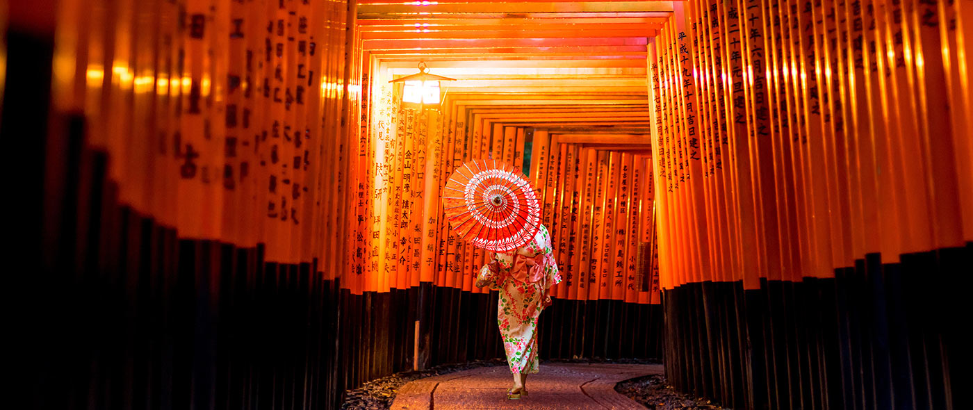 Geisha with umbrella walking through the thousands of vermilion torii gates at the Fushimi Inari Taisha shrine in Kyoto, Japan