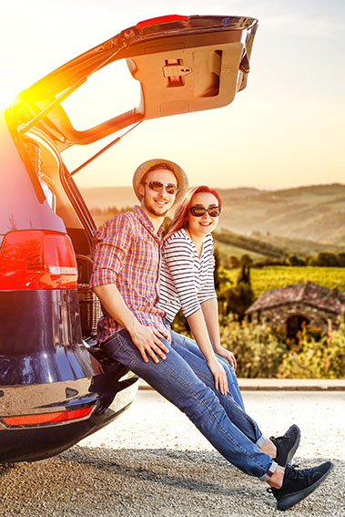 Image of two people sitting on the back of an SUV in the sun.