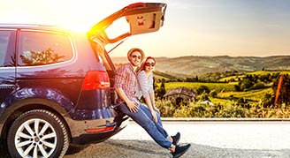 Image of two people sitting on the back of an SUV in the sun.